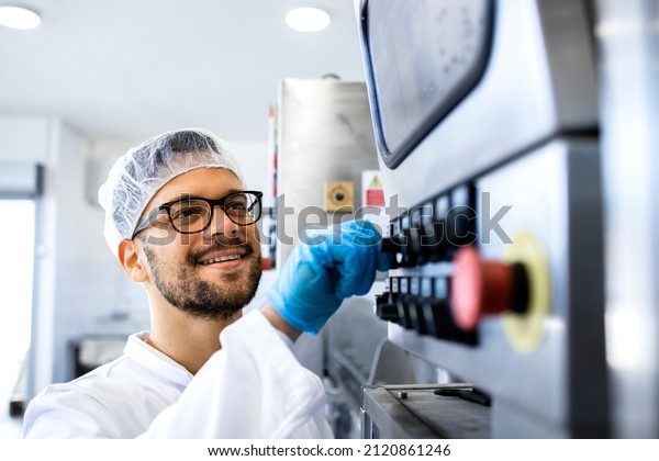 Food factory worker in sterile\
uniform and hairnet operating industrial production\
machine.