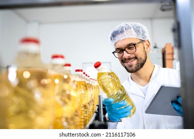 Food Factory Worker Or Technologist In White Lab Coat And Hairnet Standing By Automated Production Machine And Checking Quality Of Bottled Vegetable Oil Production.