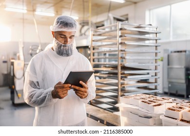 A Food Factory Worker Using Tablet And Checking On Cookies.