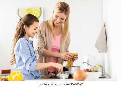 Food, Family And People Concept - Happy Mother And Daughter Cooking And Boiling Spaghetti Pasta For Dinner At Home Kitchen