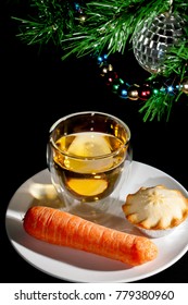 Food For Father Christmas. Mince Pie, Drink And Carrot For The Reindeer Under The Decorated Christmas Tree. Close Up Against Black Background.