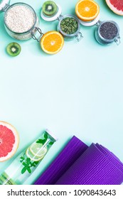 Food for fitness, healthy lifestyle frame flatlay with fat burning fruits orange and grapefruits slices, complex carbohydrates, detox water bottle, violet yoga mat, pink hand weights, green background