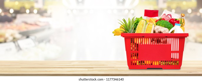 Food and groceries in shopping basket on wood table with blurred suppermarket in background, panoramic banner with copy space - Shutterstock ID 1177346140