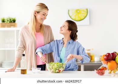 food, healthy eating, family and people concept - happy mother and daughter cooking vegetable salad for dinner at home kitchen