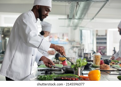 Food industry worker preparing meal in restaurant professional kitchen. Skilled head chef stirring with spatula in pan while cooking gourmet dish for dinner service, garnished with fresh herbs. - Powered by Shutterstock