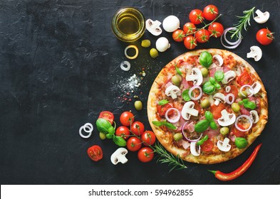 Food ingredients and spices for cooking mushrooms, tomatoes, cheese, onion, oil, pepper, salt, basil, olive and delicious italian pizza on black concrete background. Copyspace. Top view