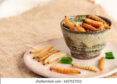 Food Insects: Bamboo worm or Bamboo Caterpillar insect fried crispy for eating as food items in bowl and plate ceramic on sackcloth, it is good source of protein edible for future food concept.