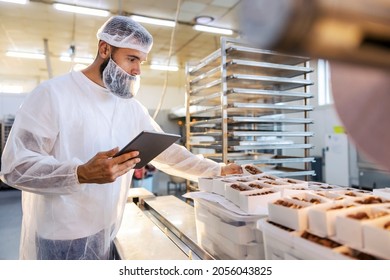 A food inspector in a sterile white uniform is holding the tablet and looking at collected cookies. Food check is important if we want quality and healthy food. - Powered by Shutterstock