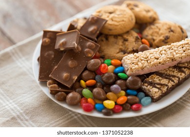 food, junk-food and unhealthy eating concept - close up of chocolate, oatmeal cookies, drop candies and muesli bars on plate