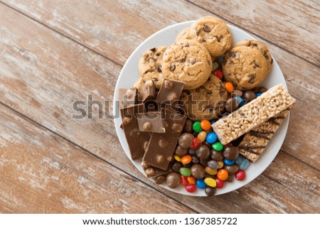 food, junk-food and unhealthy eating concept - close up of chocolate, oatmeal cookies, drop candies and muesli bars on plate