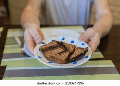 Food Mishaps. Female Hands Hold Out Plate Of Burnt Bread To Man Waiting For Food. Inexperienced Hostess Burned Bread. Burnt Food. Fried Foods Are Unhealthy. Carcinogens In Fried Foods