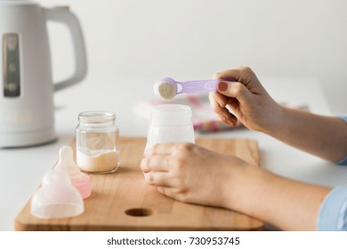 Food And Nutrition Concept - Mother Hands With Baby Bottle And Scoop Preparing Infant Formula Milk