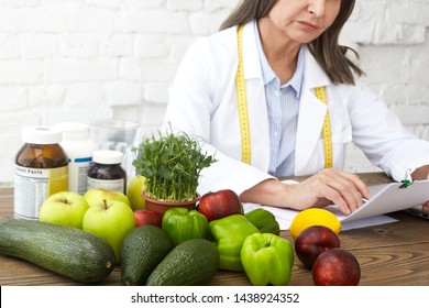 Food, Nutrition, Health, Wellbeing And Dietology Concept. Elderly Female Nutritional Expert With Measuring Tape Around Her Neck Developing Dietary Plan To Improve Eating Habits Of Her Client