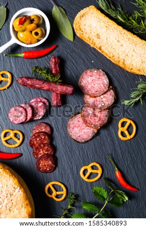 Food party background kind of cured meat Saucisson french salami, olive, prezels and homemade bread on black slate stone 