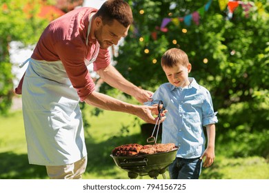 food, people and family time concept - father and son cooking meat on barbecue grill at bbq party in summer garden