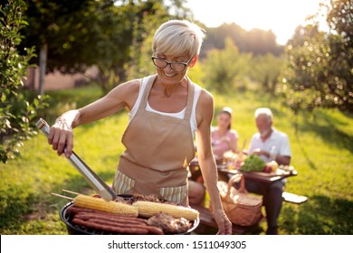 Food, People And Family Time Concept.Senior Woman Cooking Meat On Barbecue Grill At Summer Party.