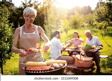 Food, People And Family Time Concept.Senior Woman Cooking Meat On Barbecue Grill At Summer Party.