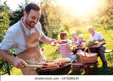 Food, People And Family Time Concept.Young Man Grilling Sausages On Barbecue At Summer Garden Party .