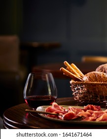 Food Photography Of A Charcuterie Board With A Glass Of Red Wine In A Stemless Glass, A Basket Of Bread And A Blurred Restaurant In The Background