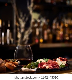 Food Photography Of A Charcuterie Board With A Glass Of Red Wine In A Stemless Glass And A Blurred Bar In The Background