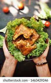 Food Photography. Chicken Wings With Lettuce In A Plate On A Black Background. Appetizing Grilled Meat, Barbecue. Tasty Dinner. A Man Holding A Plate Of Chicken Meat. Food In The Hand