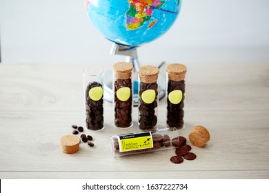 Food Photography Of Different Types Of Single Origin Chocolate Buttons In Glass Vials With Cork Stoppers On A Light Ash Timber Surface With A Globe Of The World Against A White Background