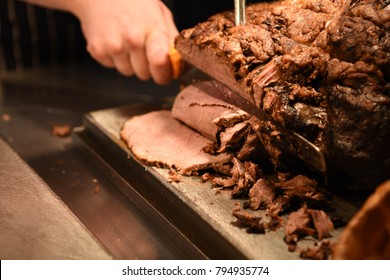 Food Photography Image With Cooked Roast Beef Joint Of Meat Being Sliced On A Board With Hand Holding The Carving Knife And A Fork Shown On A Blur Dark Background