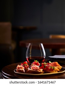 Food Photography Of A Platter Of Mixed Bruschetta With A Stemless Wine Glass Of Light Red Wine With A Bar In The Background