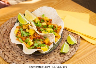 Food plated shot of two tacos pastor mexican style with jackfruit, pineapple, lime, parsley, onion and spices with napkins lime slices and wooden table.