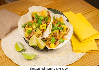 Food plated shot of two tacos pastor mexican style with pork, pineapple, lime, parsley, onion and spices with napkins lime slices and wooden table.