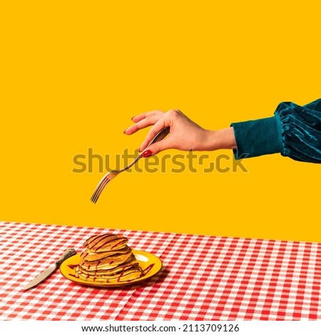 Food pop art photography. Female hand and sweet pancakes on plaid tablecloth isolated on bright yellow background. Vintage, retro 80s, 70s style. Complementary colors, Copy space for ad, text