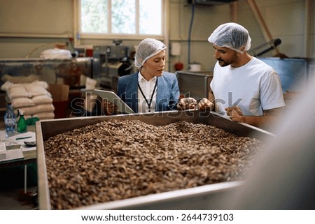 Food processing plant manager and worker examining containers with sunflower seeds.