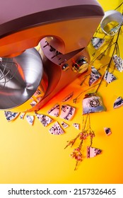 The Food Processor Stands On A Yellow Background, Decorative Fragments Of Dishes And Twigs With Small Pink Flowers Lie In A Circle