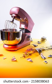 The Food Processor Stands On A Yellow Background, Decorative Fragments Of Dishes And Twigs With Small Pink Flowers Lie In A Circle