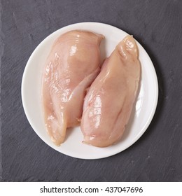 Food And Raw Meat - Uncooked Chicken Breast Fillets On A Plate, On A Rustic Slate Counter Top Background