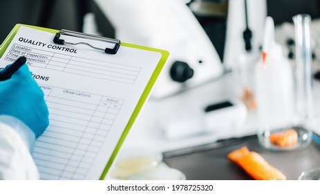 Food safety and quality management. Food safety and quality inspector filling out quality control form in a laboratory, salmon in background - Shutterstock ID 1978725320