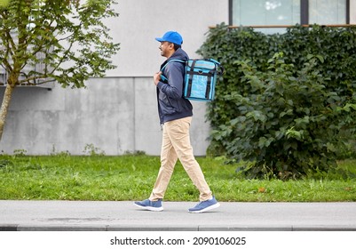 food shipping, profession and people concept - happy smiling delivery man with thermal insulated bag walking along city street