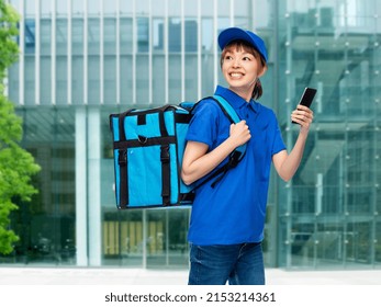 Food Shipping, Profession And People Concept - Happy Smiling Delivery Woman With Thermal Insulated Bag And Smartphone Over Office Building On City Street Background