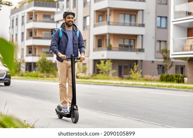 food shipping, transportation and people concept - happy smiling delivery man in bike helmet with thermal insulated bag riding electric scooter on city street