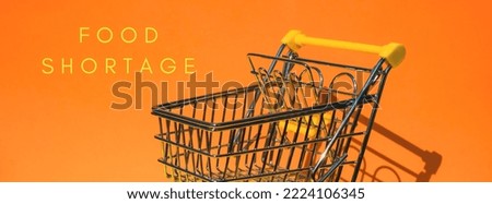 FOOD SHORTAGE text Empty shopping trolley cart on colorful orange background. Online shopping, buy mall market shop consumer concept. Small toy supermarket grocery push cart. Rising food cost, grocery