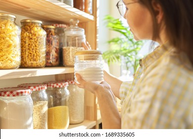 Food Storage In Pantry, Woman Holding Jar Of Sugar In Hand. Pantry Interior, Wooden Shelf With Food Cans And Kitchen Utensils