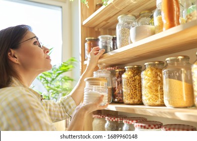 Food Storage In Pantry, Woman Holding Jar Of Sugar In Hand. Pantry Interior, Wooden Shelf With Food Cans And Kitchen Utensils