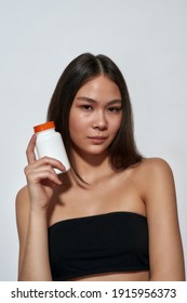 Food Supplements For Healthy Skin. Young Beautiful Asian Woman Holding Container With Vitamins And Looking At Camera, Standing Against Light Background. Healthy Lifestyle, Wellness And Beauty Concept