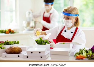 Food Takeaway In Restaurant In Coronavirus Outbreak. Cafe Staff In Face Mask And Shield Cooking Takeout Order. Safety, Covid-19 Prevention. Chef With Salad In Cardboard Container, Eco Friendly, Vegan.