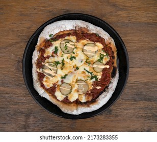 Food. Top View Of A Pizza With Minced Meat, Tomato Sauce, Grilled Cucumber, Garlic Aioli And Chives, In A Black Pizza Pan On The Wooden Table. 