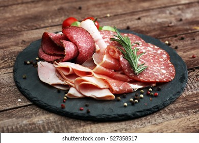 Food tray with delicious salami, pieces of sliced ham, sausage, tomatoes, salad and vegetable - Meat platter with selection - Cutting sausage and cured meat on a celebratory table. - Powered by Shutterstock