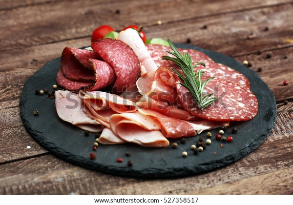 Food tray with delicious salami, pieces of sliced\
ham, sausage, tomatoes, salad and vegetable - Meat platter with\
selection - Cutting sausage and cured meat on a celebratory\
table.