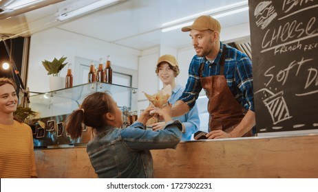 Food Truck Employee Hands Out a Freshly Made Burger to a Happy Young Female. Young Lady is Paying for Food with Contactless Credit Card. Street Food Truck Selling Burgers in a Modern Hip Neighbourhood - Powered by Shutterstock