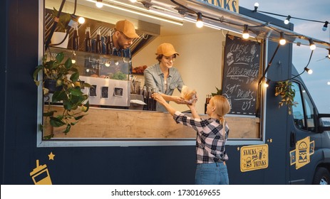 Food Truck Employee Hands Out a Freshly Made Burger and a Soft Drink to a Happy Young Female. Street Food Truck Selling Burgers in a Modern Hip Neighbourhood - Powered by Shutterstock