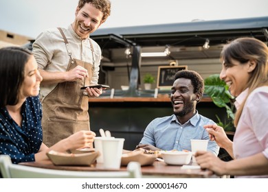 Food truck owner taking customers orders with mobile device - Happy multiracial people having a meal outdoor - Powered by Shutterstock